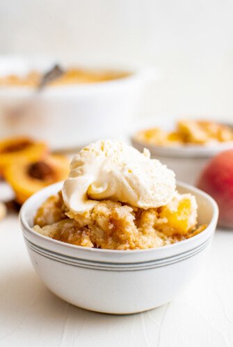 Baked peach cake topped with vanilla ice cream, in a small serving bowl.