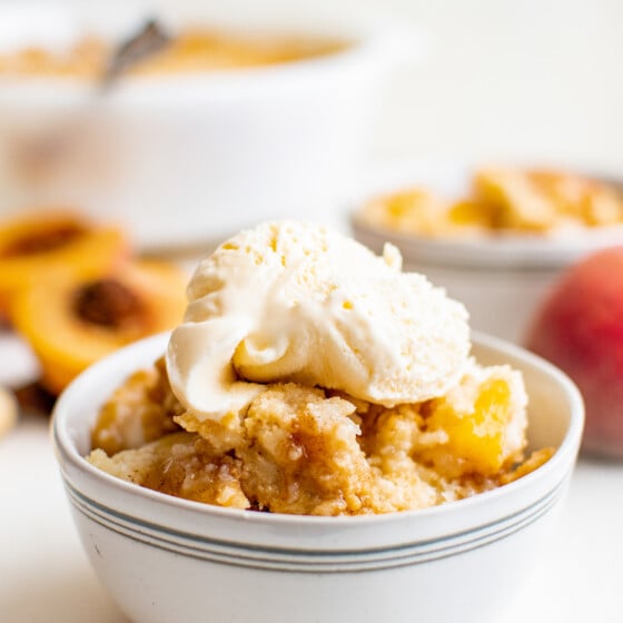 Baked peach cake topped with vanilla ice cream, in a small serving bowl.