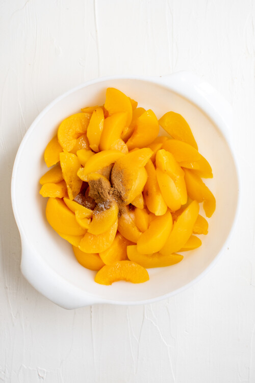 Sliced peaches in a round white baking dish, with cinnamon.