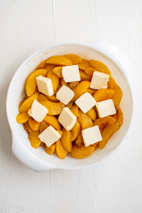 Sliced peaches in a baking dish, dotted with pats of butter.