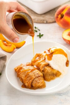 Peach dumplings in a white bowl with caramel sauce being poured on top.