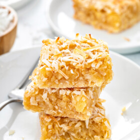 Close-up shot of pineapple coconut bars, stacked on a plate with a fork.