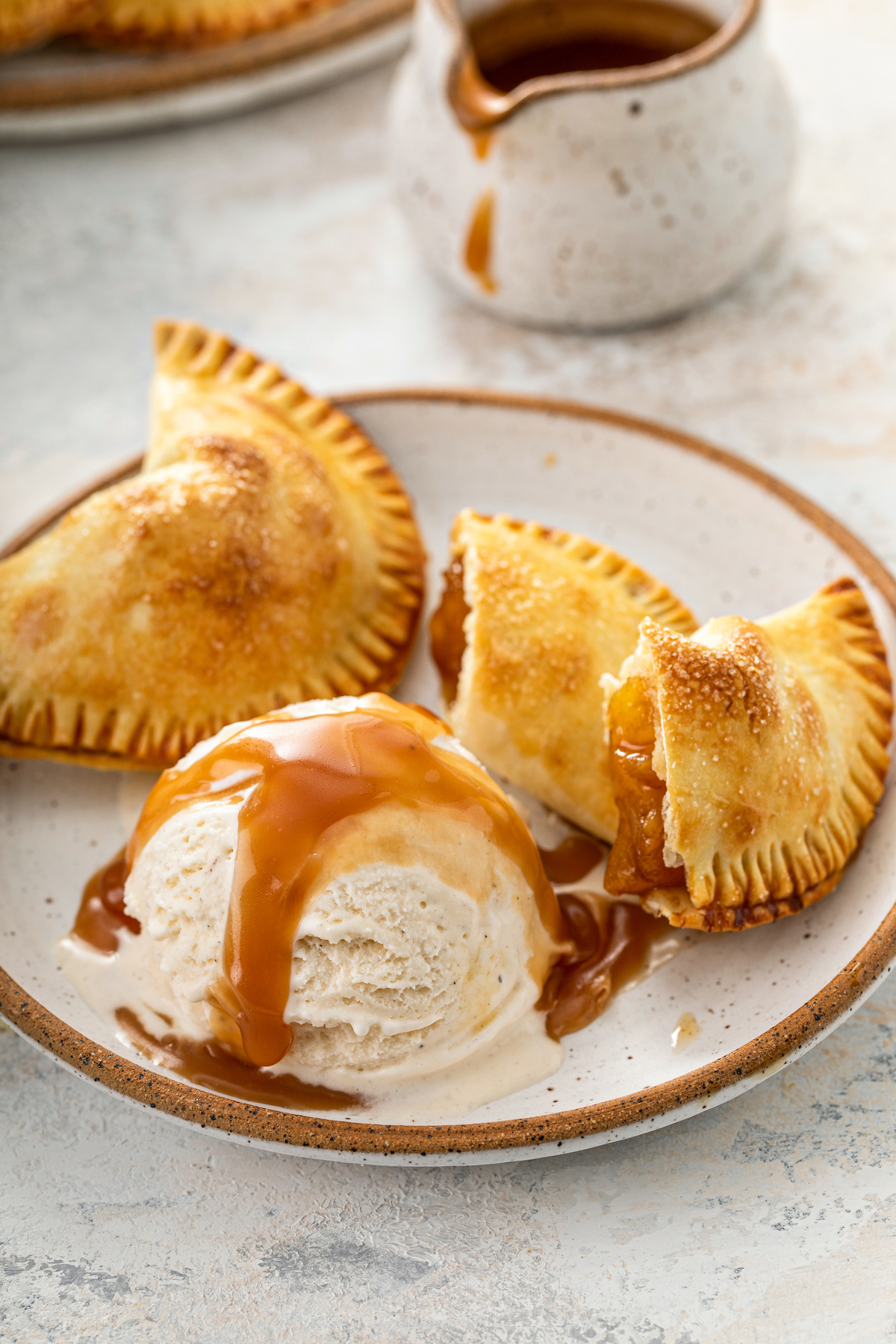 Pineapple empanadas cut in half in a bowl with ice cream and caramel sauce.