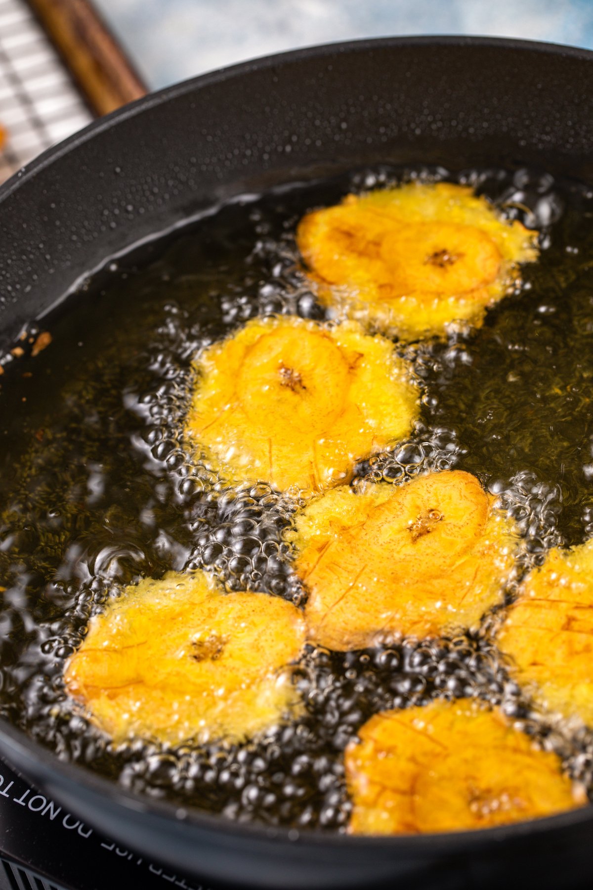 Plantains frying in oil in a skillet.