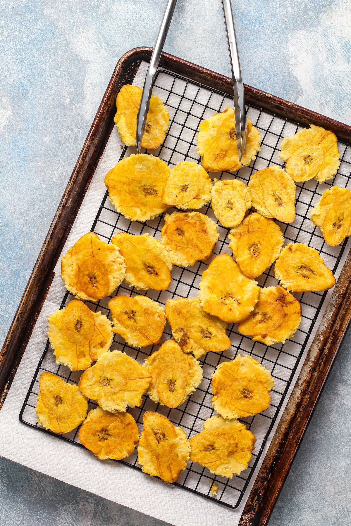 Smashed and fried plantains on a rack draining over paper towels.