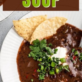 A bowl of black bean soup with cilantro, green onions and sour cream on top.