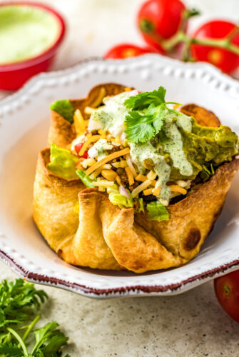 A homemade tortilla bowl filled with meat, cheese, lettuce, sour cream, and other ingredients.