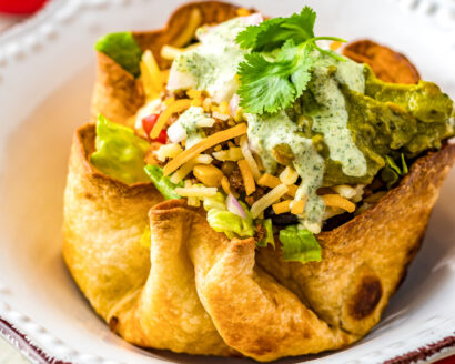 A homemade tortilla bowl filled with meat, cheese, lettuce, sour cream, and other ingredients.
