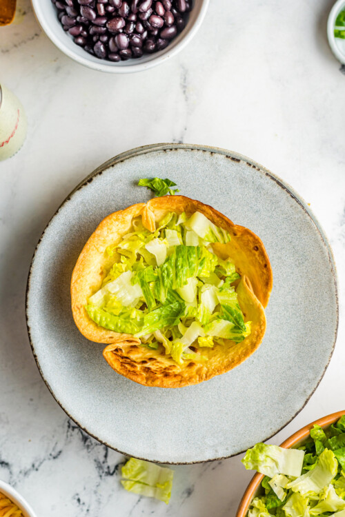 A baked tortilla bowl with lettuce in the bottom.