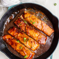 Salmon fillets in a brown sauce, garnished with green onions.