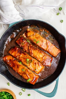 Salmon fillets in a brown sauce, garnished with green onions.