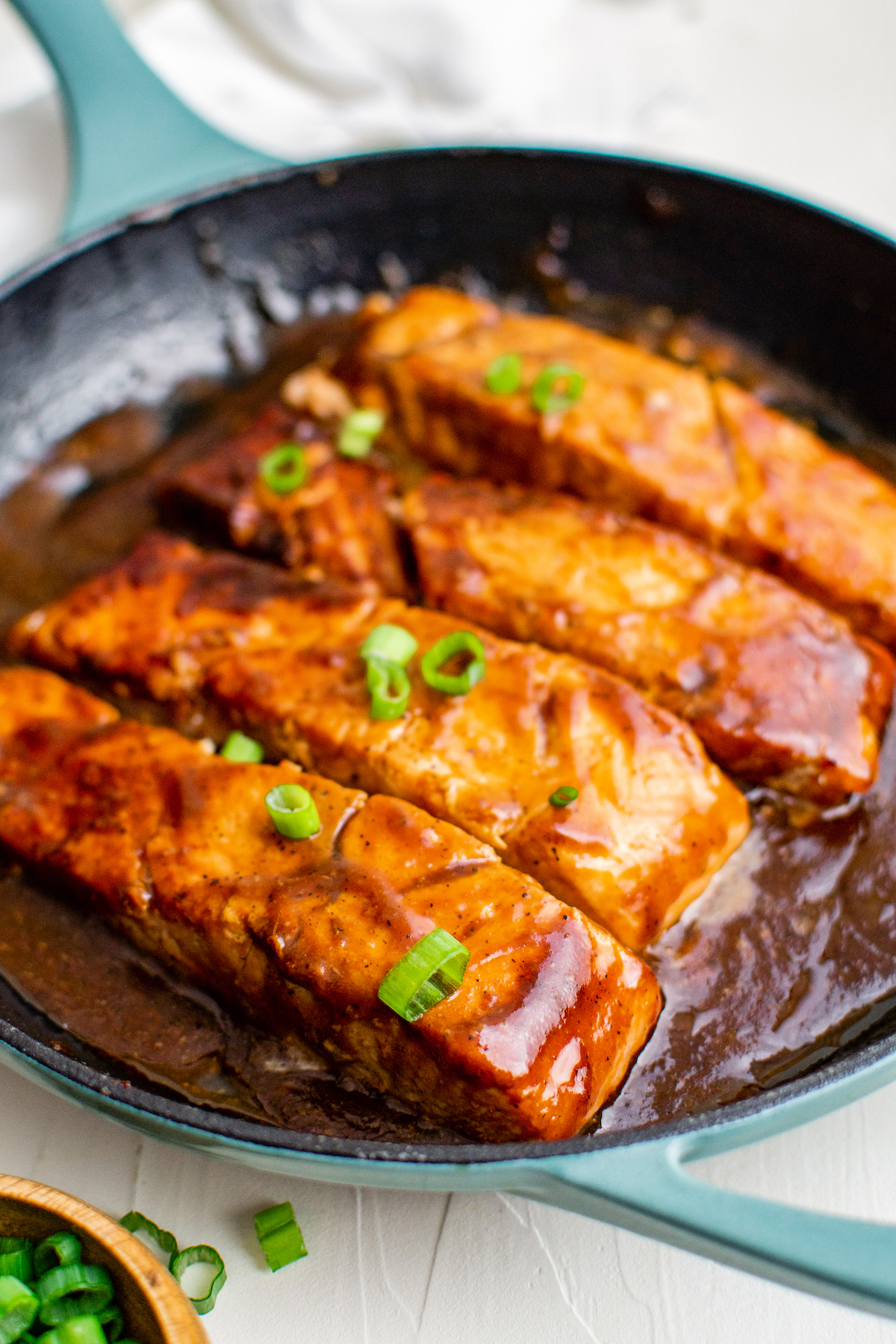 Teriyaki salmon in a skillet with lots of sauce, garnished with sliced green onio.