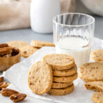 Crisp shortbread cookies stacked on a plate with milk and additional cookies.