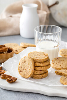 Crisp shortbread cookies stacked on a plate with milk and additional cookies.