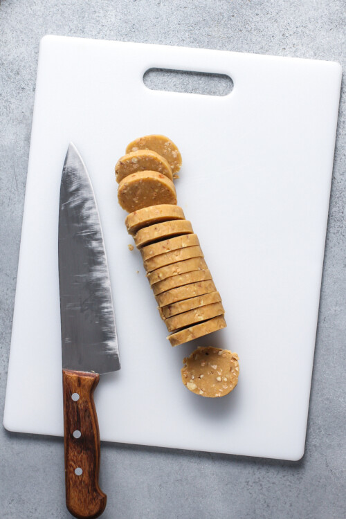Cookie dough cut into slices on a cutting board with a large knife lying nearby.