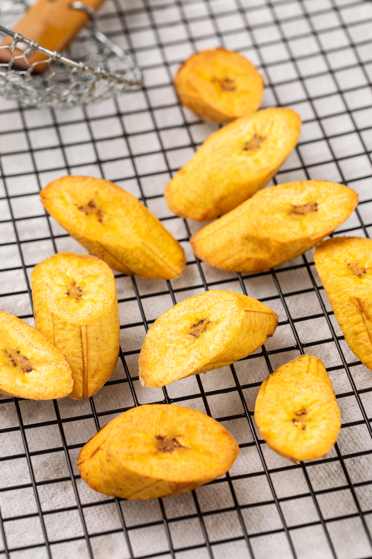 Plantain pieces fried and draining on a cooling rack.
