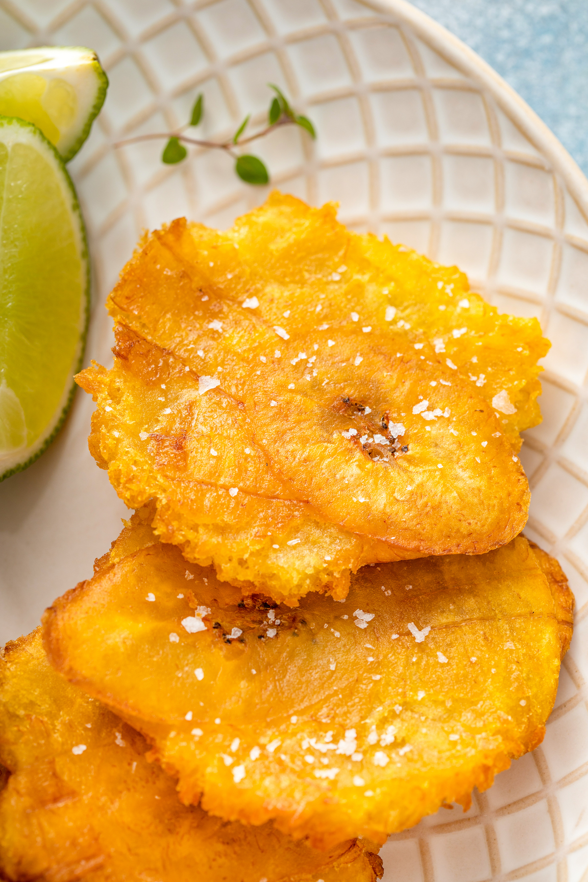 Up close image of smashed fried plantains on a plate with salt sprinkled on top.