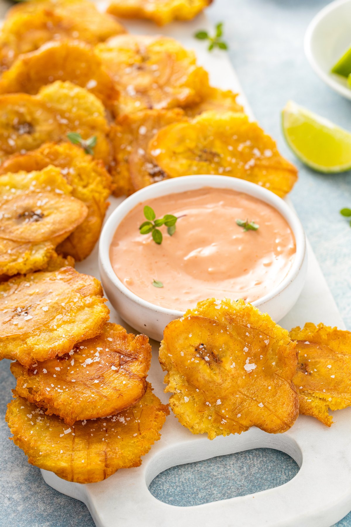 Fried plantains on a serving platter with salt on top with a bowl of mayo ketchup sauce for dipping.