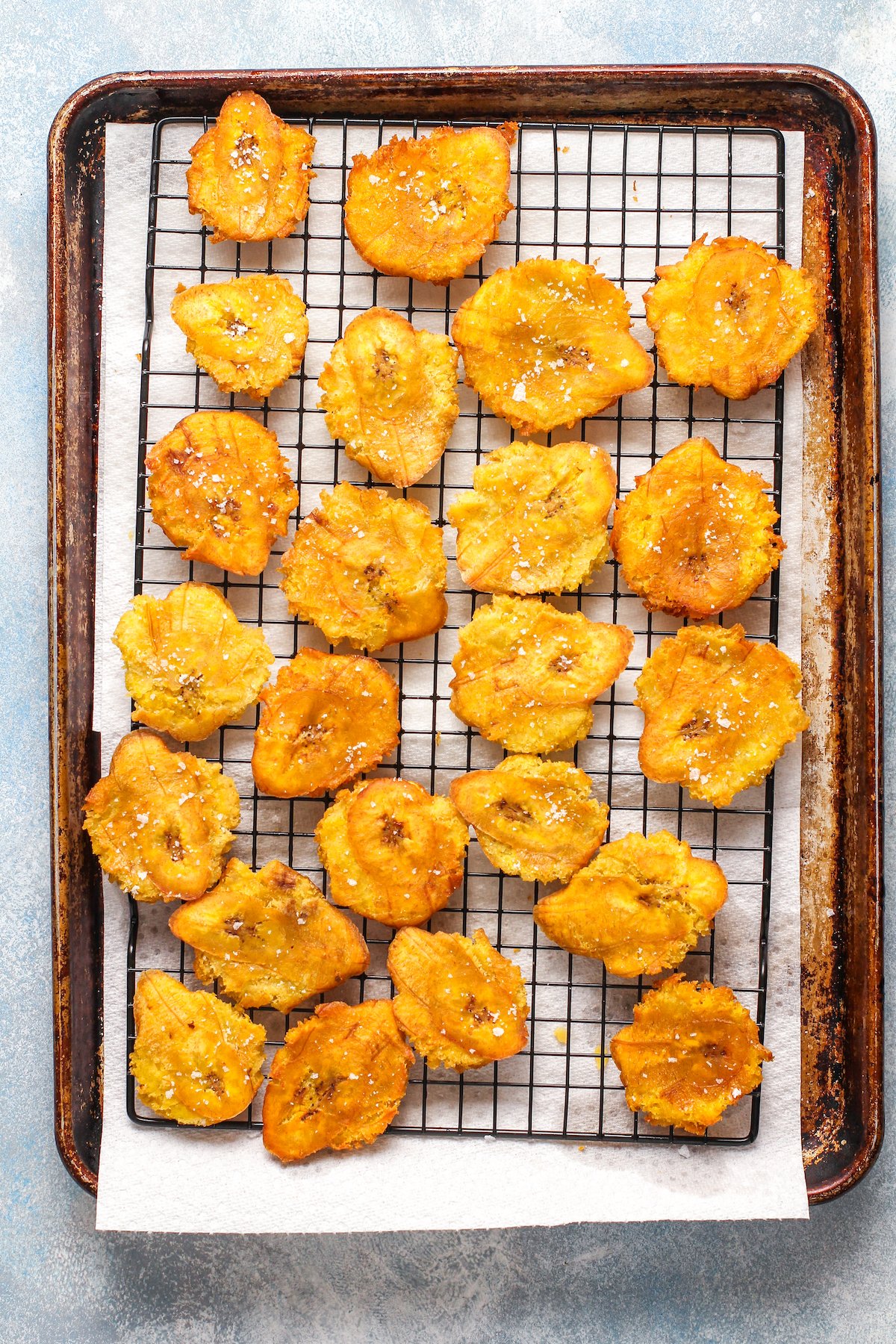 Tostones sprinkled with salt on a cooling rack over paper towels to catch grease.