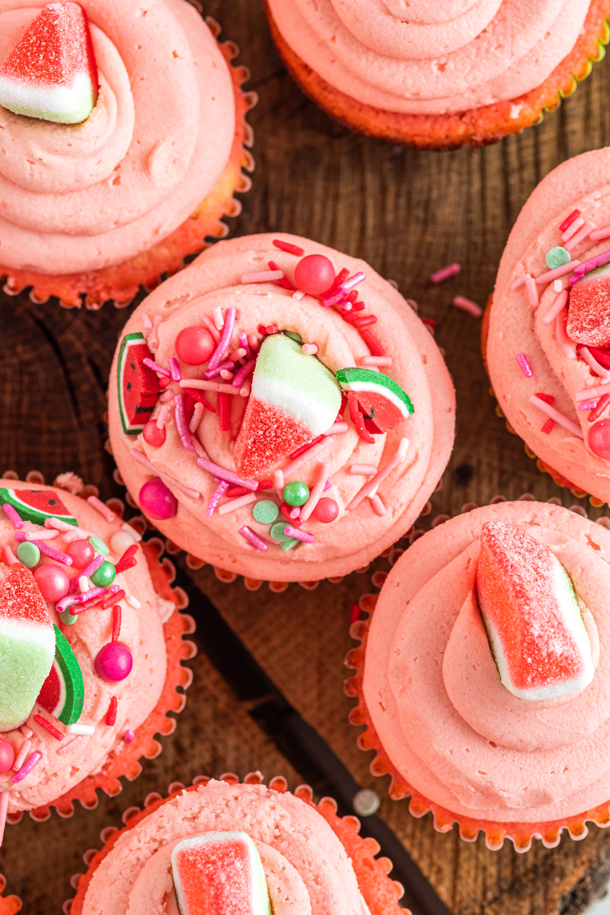 Close up top view of pink frosted watermelon cupcakes decorated with sprinkles and watermelon candy.