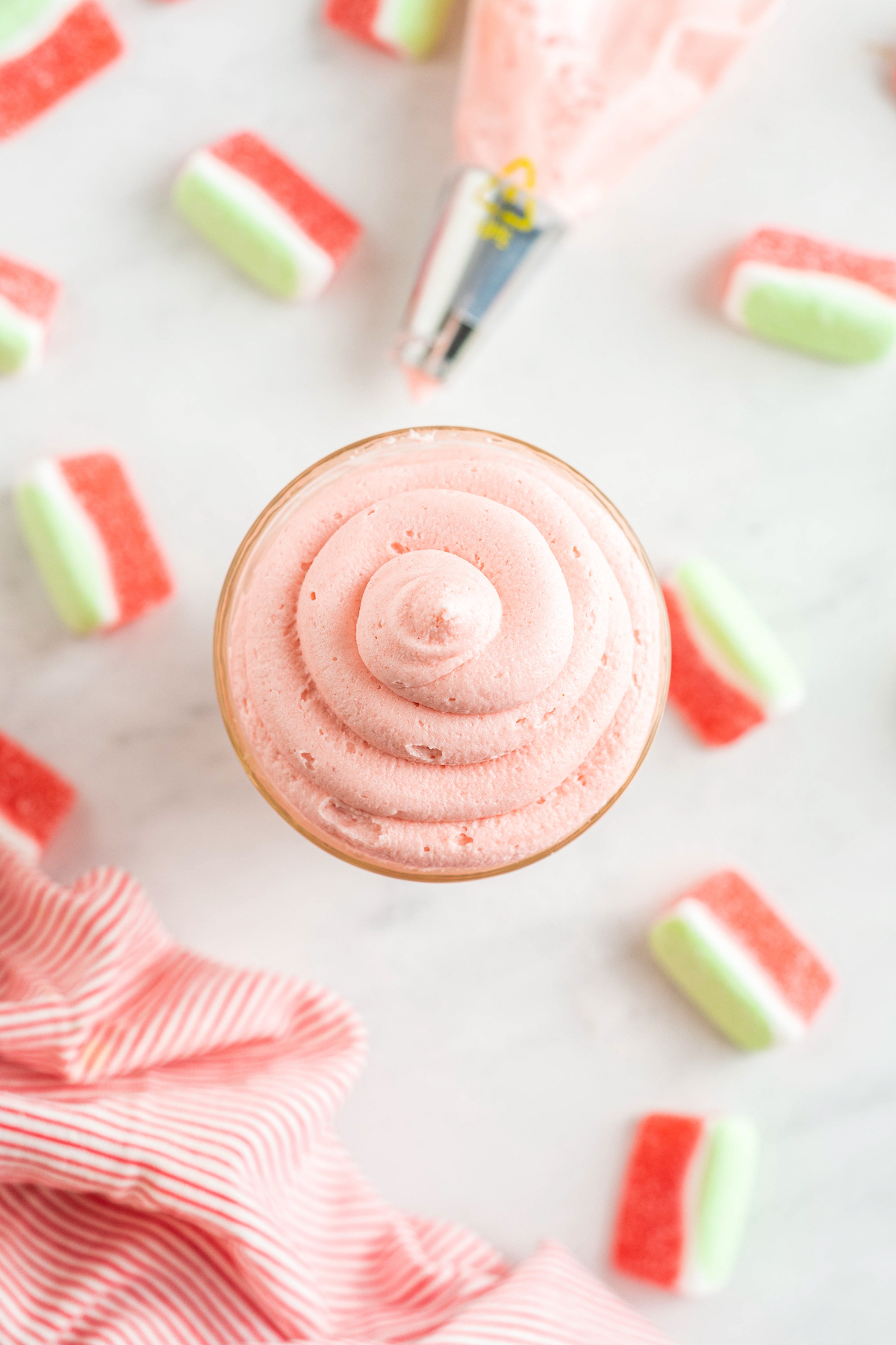 Top view of pink watermelon buttercream swirled inside a glass, next to scattered watermelon candies.