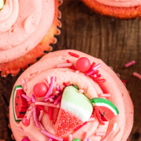 Watermelon frosting on a cupcake with sprinkles.