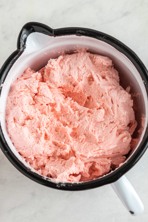 Close up top view of a large measuring cup filled with pink watermelon buttercream.