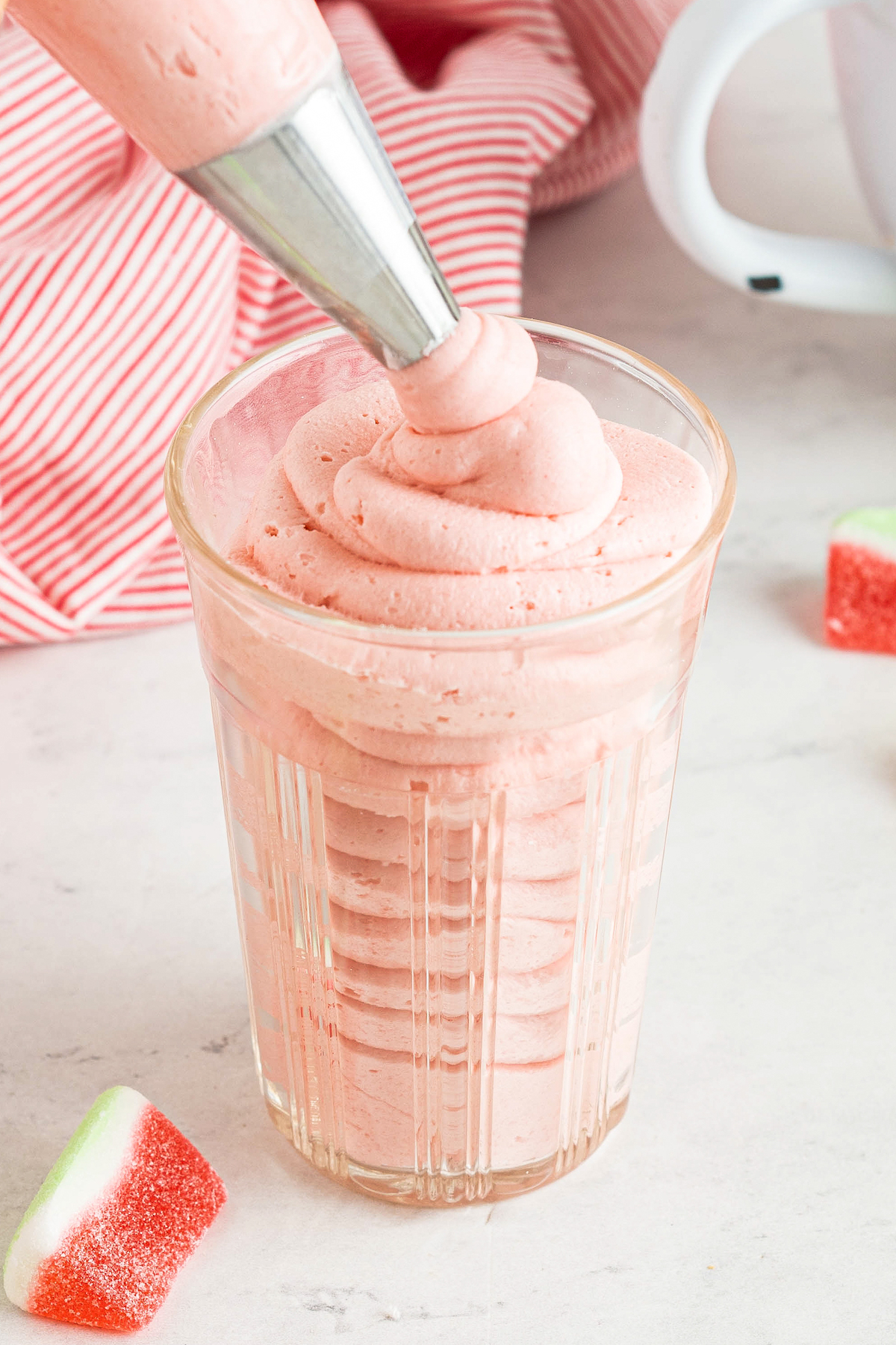 Pink watermelon buttercream is piped into a glass with a piping bag.