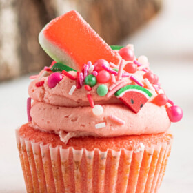 A single pink watermelon cupcake with watermelon buttercream and watermelon sprinkles and candy on top.