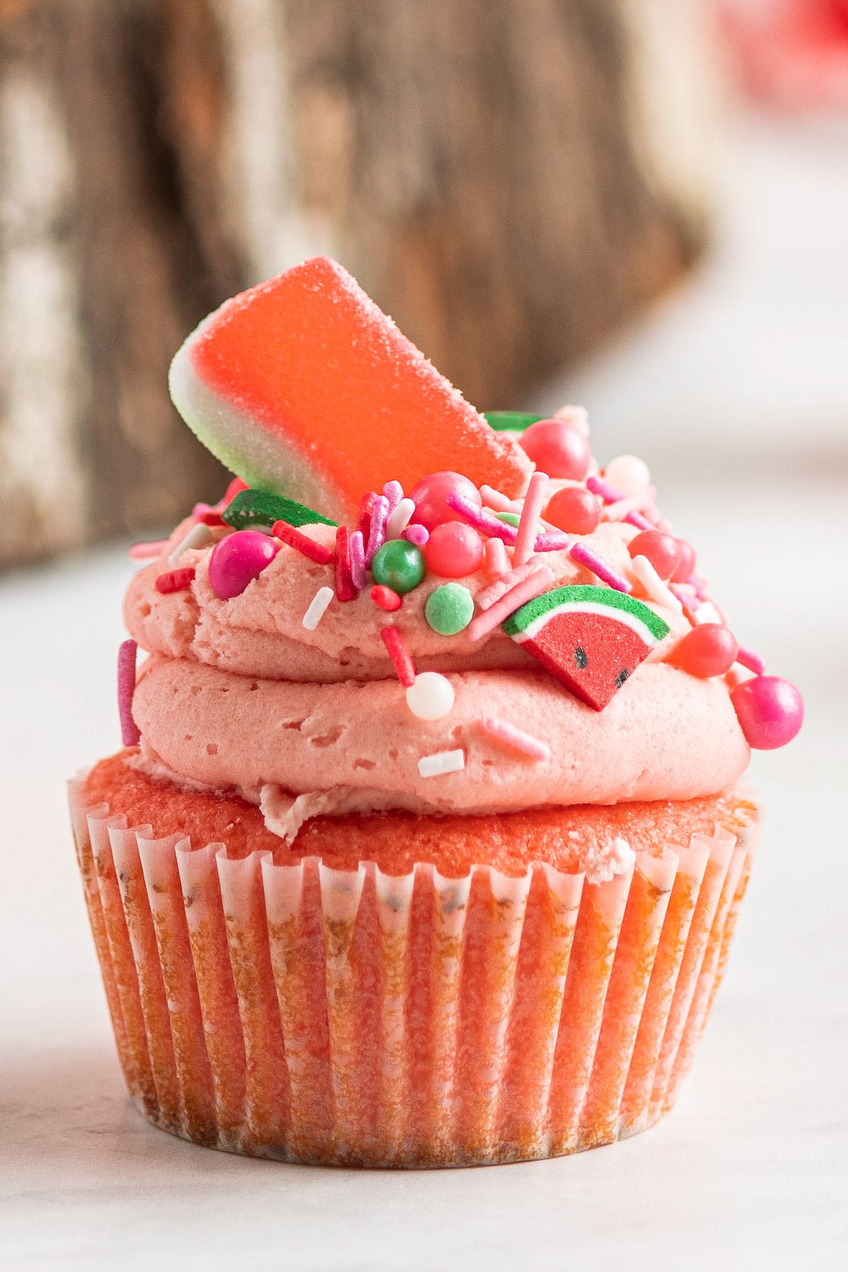 A single pink watermelon cupcake with watermelon buttercream and watermelon sprinkles and candy on top.