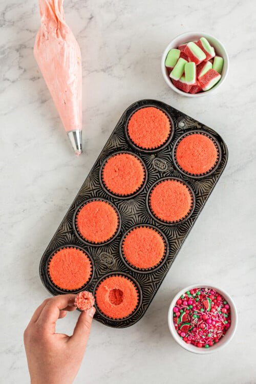 Top view of a hand removing the center from one watermelon cupcake in a full cupcake pan.