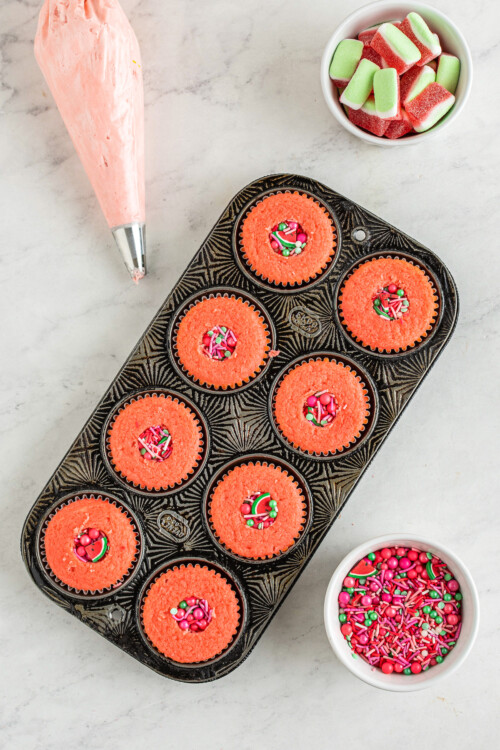 Top view of watermelon cupcakes in a cupcake pan with their centers removed and replaced with colorful sprinkles.