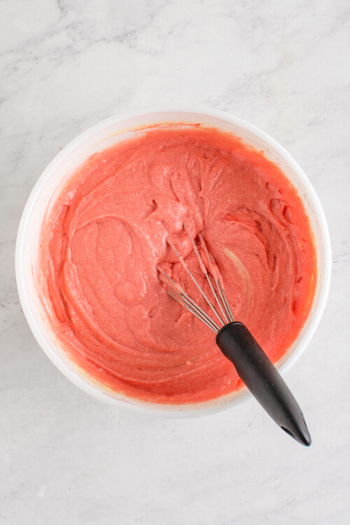Bright pink watermelon cupcake batter in a mixing bowl with a whisk.