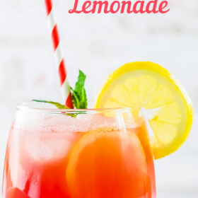 A glass of watermelon lemonade with a red and white striped straw, fresh mint and lemon garnish.