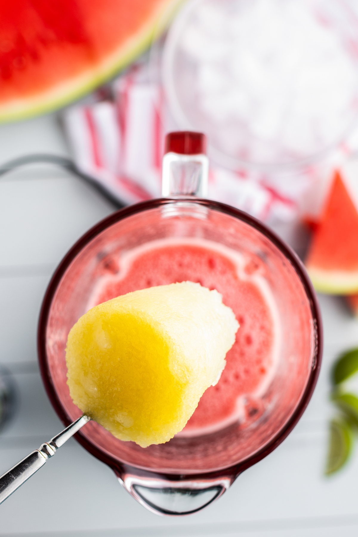 Top view of frozen limeade being added into a blender with watermelon juice.