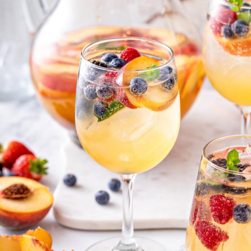 A glass of white sangria with blueberries, strawberries, and peaches.