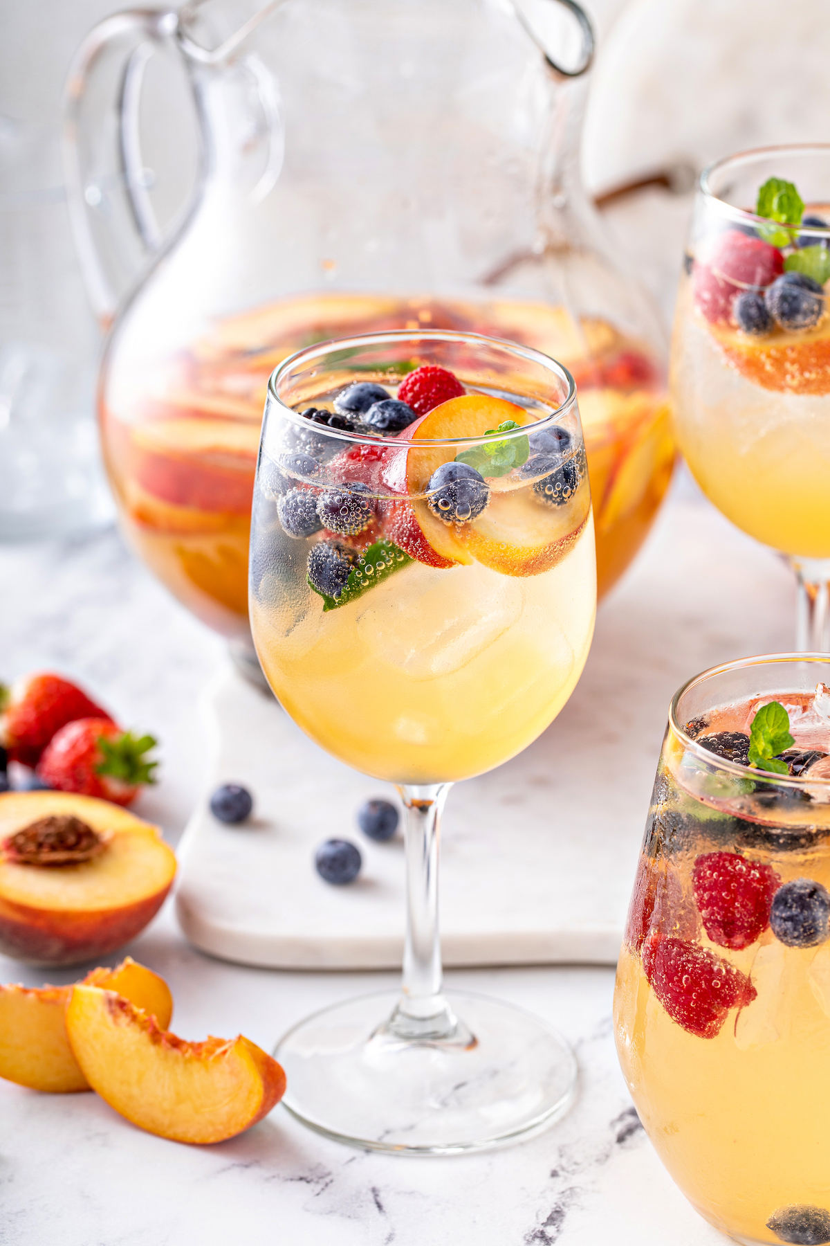 A glass of white sangria with blueberries, strawberries, and peaches.
