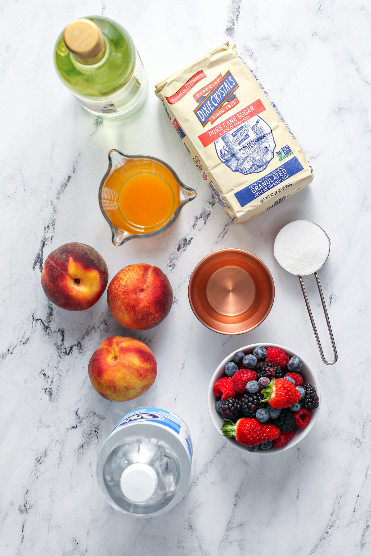 From top left: A bottle of white wine, sugar, peach nectar, fresh peaches, peach schnapps, mixed berries, seltzer.