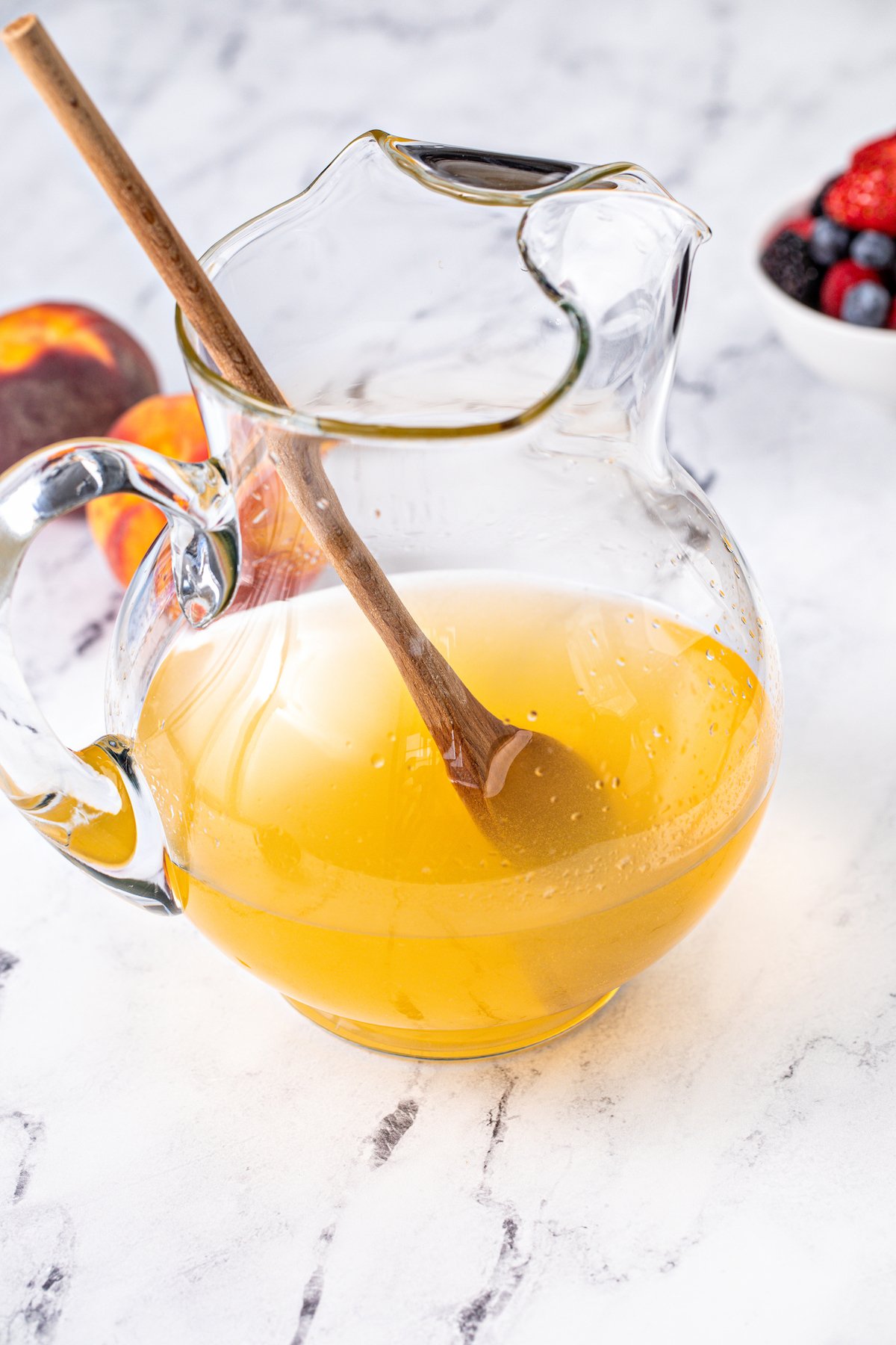 A pitcher of white wine, peach nectar, sugar, and peach schnapps, with a wooden spoon resting inside.