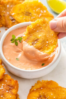 Tostones being dipped into a bowl of mayo ketchup.
