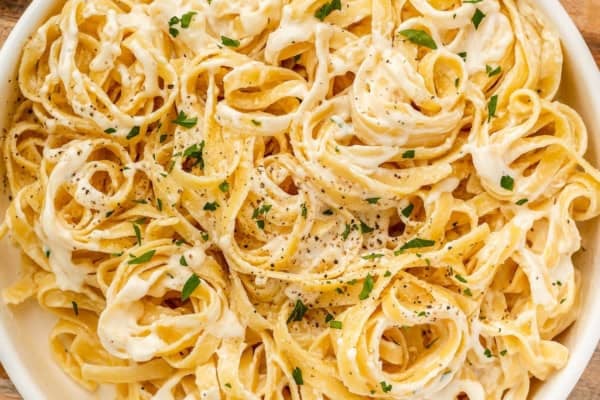 A close-up of creamy fettuccine Alfredo pasta made with rich Alfredo sauce with cream cheese, garnished with chopped parsley and ground black pepper, served in a white bowl.