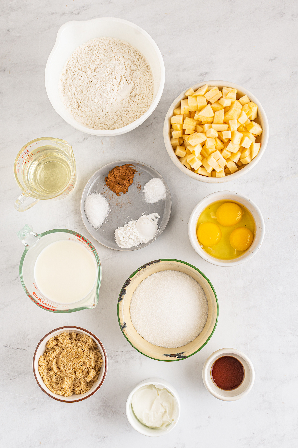 From top left: Flour, chopped apple, vegetable oil, cinnamon, salt, baking soda, baking powder, eggs and an extra egg yolk, milk, sour cream, brown sugar, vanilla,