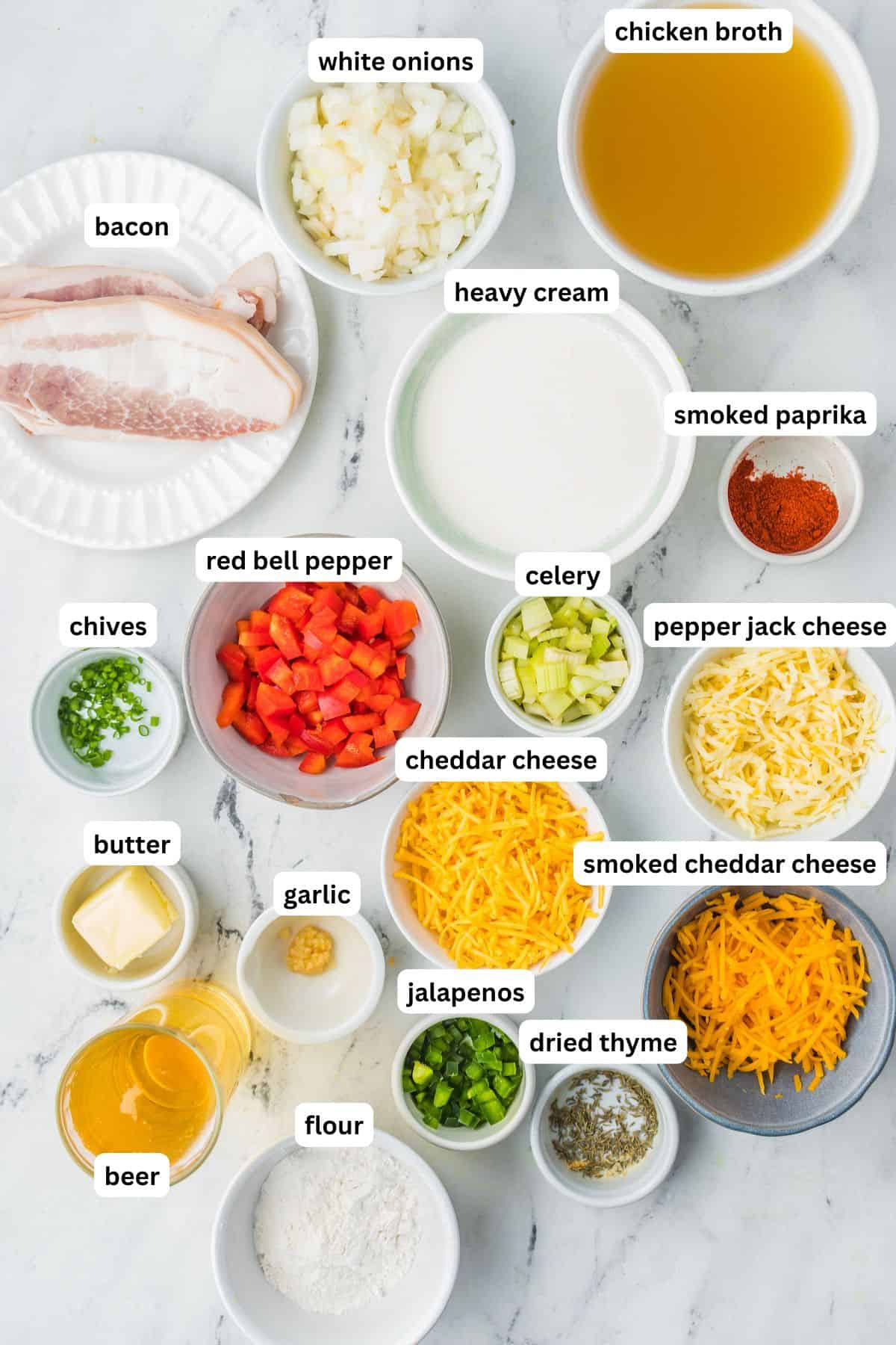 Ingredients for beer cheese soup recipe in order from top to bottom: bacon, white onions, chicken broth, heavy cream, smoked paprika, chives, red bell pepper, celery, pepper jack cheese, butter, garlic, cheddar cheese, smoked cheddar cheese, beer, flour, jalapeños, dried thyme.