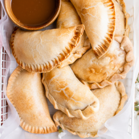 Apple empanadas on a sheet of parchment paper with a bowl of caramel sauce.