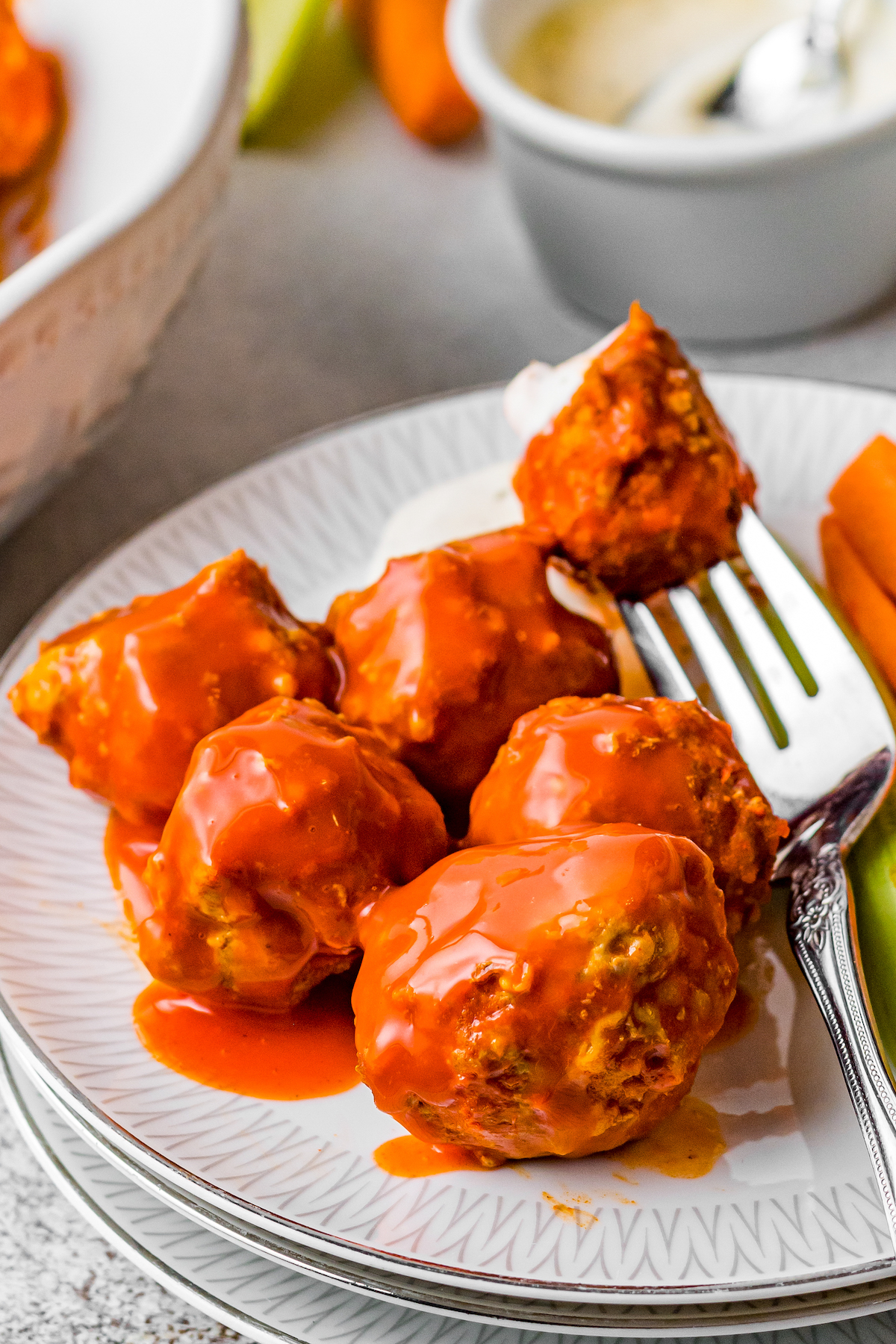 Chicken meatballs in a buffalo sauce on a white plate with a fork.