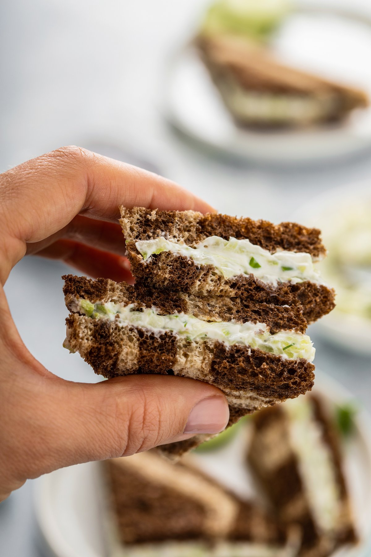 Two fingers holding a cucumber tea sandwich.