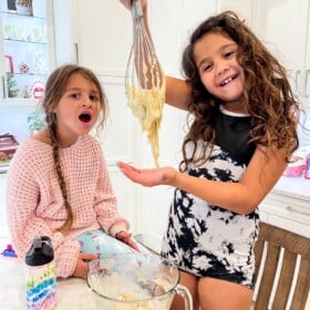 Two girls baking cookies with one girl holding a whisk.