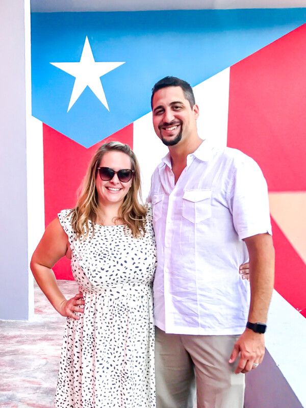 Jessica Segarra and Jorge Segarra in Puerto Rico standing side by side in front of a Puerto Rican flag at a restaurant.