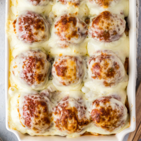 Cheese on top of meatball casserole in a white baking dish.