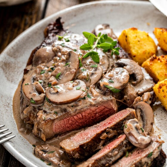 A sliced steak on a plate with mushroom sauce and roasted potatoes.